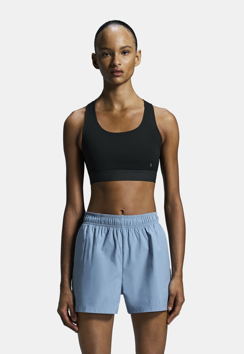 Soutien-gorge de sport noir avec un décolleté arrondi, associé à un short d'athlétisme bleu clair avec une taille élastique et une coupe ample.