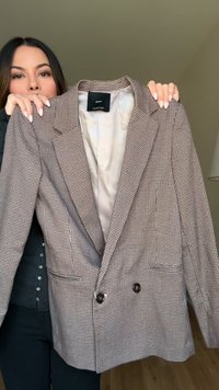 Brązowa i biała marynarka w kratę houndstooth, dwurzędowa, z wyciętym kołnierzem, dwoma guzikami i kieszeniami z przodu. Widoczne gładkie wykończenie wnętrza.