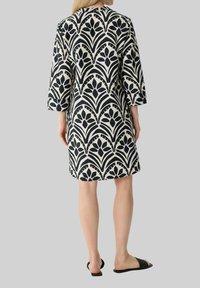 Schwarz-weißer Kleid mit Muster, das ein fließendes Design, drei Viertelärmel und einen knielangen Schnitt aufweist, gefertigt aus einem leichten Stoff.
