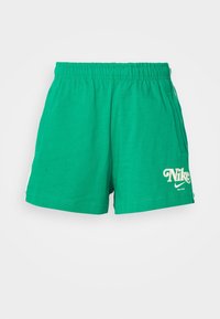 Pantaloni corti verdi in cotone con vita elastica, dotati di tasche laterali e un logo Nike color crema con la scritta "Dal 1972" stampata sotto.