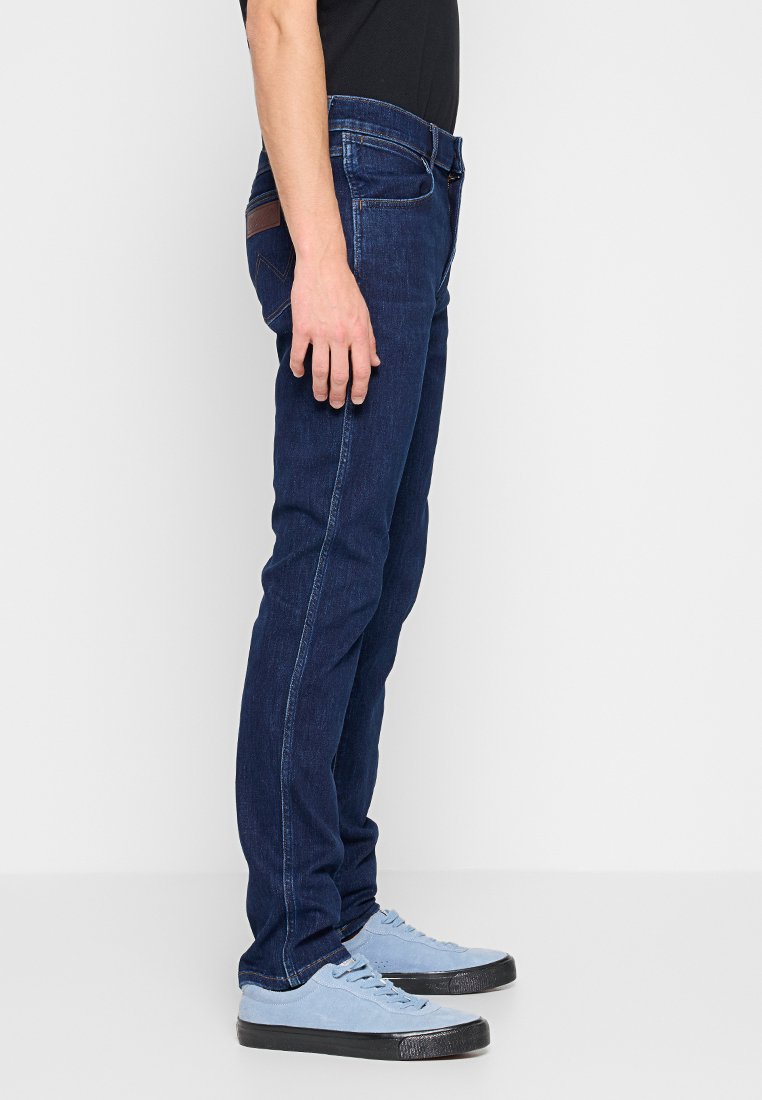 Dunkelblaue Denim-Jeans mit geradem Schnitt, ausgestattet mit fünf Taschen, kontrastierenden Nähten und einem Lederakzent auf der Gesäßtasche.