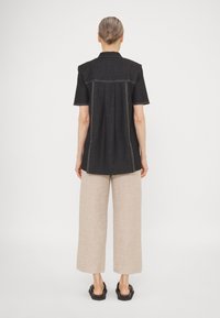 Maglietta nera a maniche corte con cuciture bianche a contrasto, dotata di un retro con yoke e una vestibilità rilassata, abbinata a pantaloni beige larghi.