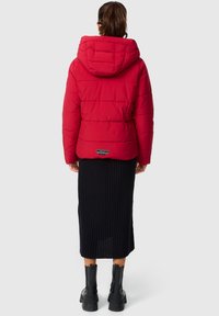 Red puffer jacket with a hood, textured surface, quilted design, paired with a black ribbed skirt and black chunky boots.