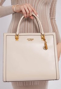 Crème leren tote bag met rechthoekige vorm, gouden accessoires en een logo. Met een sleutelhanger accent en gestructureerde handvatten.