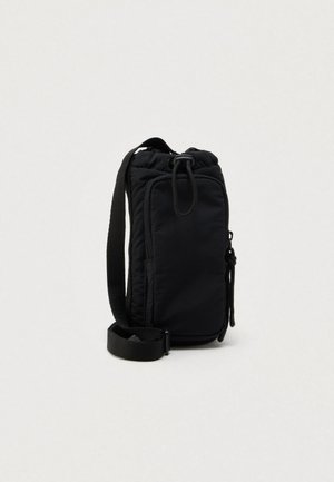 Compact zwart crossbodytasje met verstelbare schouderriem, voorvak met rits en trekkoordsluiting tegen een effen lichte achtergrond.