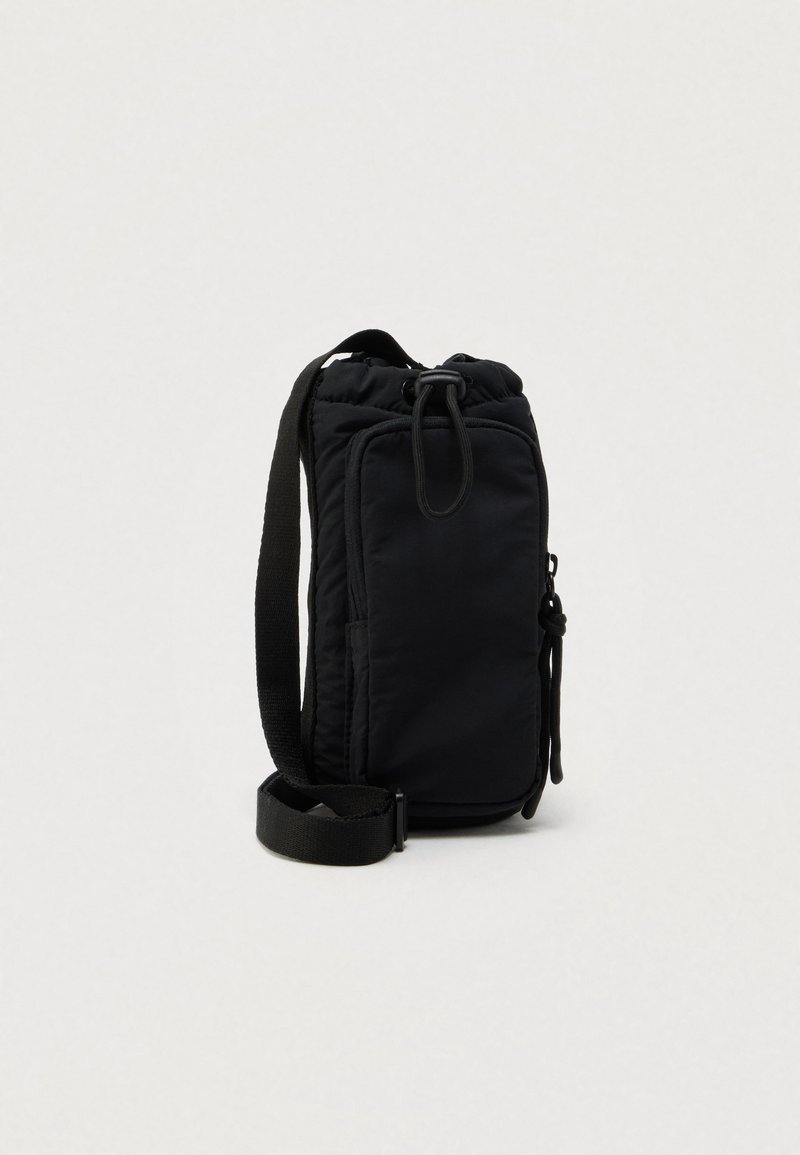 Kompaktowa czarna torebka na ramię z regulowanym paskiem, przednią kieszenią na zamek i zapięciem na sznurek na jasnym, jednolitym tle.