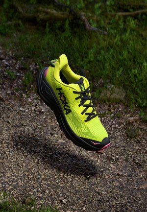 Hoka athletic shoe, neon yellow mesh upper, black rubber sole, black laces, pink accent, cushioned design, lightweight construction.