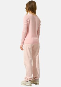 Helles rosa Strickpullover mit langen Ärmeln, figurbetontem Schnitt und rundem Ausschnitt, kombiniert mit hellrosa lockeren Hosen und grauen Turnschuhen.