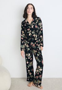 Florale zwarte pyjama set met een knoopsluiting bovenstuk met lange mouwen en bijpassende wijde broek. De stof heeft een gladde, zachte textuur.