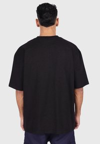Sort oversized bomulds t-shirt med korte ærmer, rund halsudskæring og en afslappet pasform. Glat tekstur og retkantet søm ved taljen.