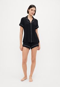 Schwarzes kurzärmliges Nachthemd mit Knöpfen und weißen Paspeln, kombiniert mit passenden schwarzen Shorts mit weißem Saum. Weicher, leichter Stoff.