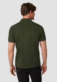 Donkergroen polo shirt met korte mouwen, kraag en een subtiel embleem op de rug. Textuurstof, casual pasvorm en een strak ontwerp.