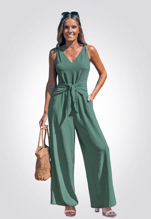 Tuta verde con gambe ampie e vita legata. Realizzato in tessuto testurizzato, presenta spalline regolabili e scollo a V. Accessorio borsa in tessuto.