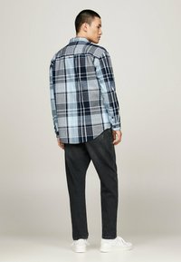 Camisa de cuadros de manga larga en tonos azul, marino y gris, con dobladillo redondeado y puños abotonados. Combinada con jeans oscuros y zapatillas blancas.