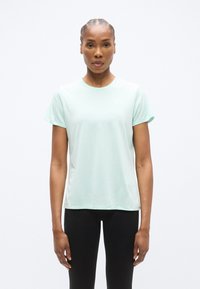 Αθλητική μπλούζα σε ανοιχτό μέντα πράσινο με στρογγυλή λαιμόκοψη και κοντά μανίκια, κατασκευασμένη από απαλό, αναπνεύσιμο ύφασμα, σε συνδυασμό με μαύρο κολάν.