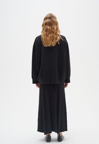 Sudadera negra oversize con textura acanalada, combinada con una larga falda negra. Diseño simple, hardware minimalista y botas hasta el tobillo.