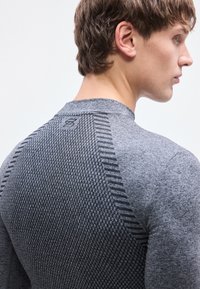 Γκρι αθλητική μπλούζα με υφασμάτινο σχέδιο στην πλάτη, με ριμπ λεπτομέρειες και εφαρμοστή γραμμή, που δείχνει μέρος του λαιμού και του ώμου ενός ατόμου.