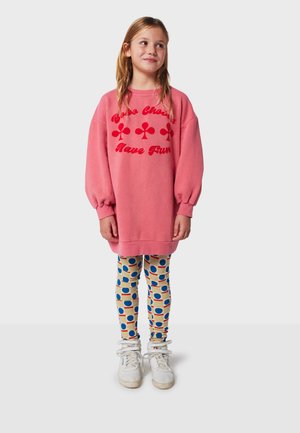 Pink sweatshirt dress with red text and floral patterns, paired with patterned leggings featuring blue circles on a beige background and white sneakers.