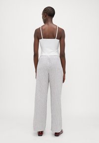 Top a spalla bianca con spalline sottili abbinato a pantaloni larghi con un motivo a righe verticali in grigio chiaro e grigio scuro.