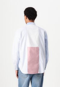 Camicia a righe blu e bianca con un pannello rosa a contrasto sul retro, caratterizzata da un colletto classico e maniche lunghe.