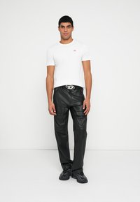 Bijela majica kratkih rukava s malim crvenim logotipom, uparena s crnim kožnim hlačama s patentnim zatvaračima i remenom sa srebrnom kopčom.