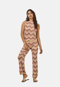 Conjunto de dos piezas de punto que incluye una blusa sin mangas y pantalones acampanados con un patrón de zigzag en tonos rosa y beige. Destacado por una textura ligera.
