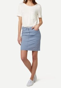 Falda de mezclilla azul clara con un diseño ajustado, bolsillos laterales y detalles de costura. Combinada con una blusa blanca de manga corta. Zapatillas blancas.