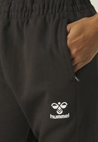 Pantaloni da tuta neri con vita elasticizzata e tasca laterale. Presenta un logo bianco all'altezza dell'anca. Realizzati in tessuto morbido e liscio.