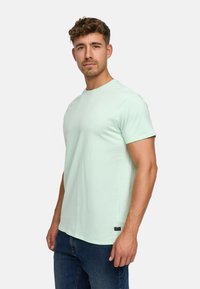 Light mint green short-sleeve t-shirt made of cotton, featuring a round neckline and a small logo accent on the chest. Denim jeans visible below.