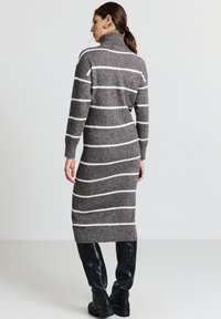 Abito a maglia grigio a righe con colletto alto, caratterizzato da righe orizzontali bianche e polsini a costina. Abbinato a stivali neri lucidi al ginocchio.