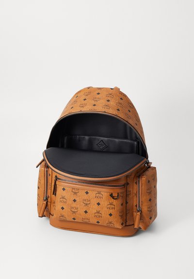 Zaino in pelle marrone con motivo logo MCM, doppie cerniere e interno nero. Presenta una parte superiore arrotondata e tasche frontali con cerniera.