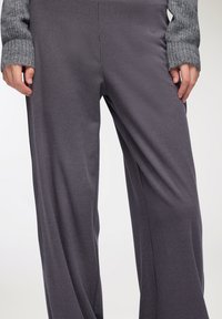 Szare, strukturowane spodnie z szerokimi nogawkami w małą kratkę. Tkanina delikatnie opada, uwydatniając ruch. Rękawy swetra dzianinowego widoczne na nadgarstkach.