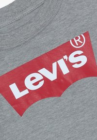 Tissu gris avec un grand logo Levi's rouge et blanc imprimé près de l'encolure montrant le symbole de marque déposée.