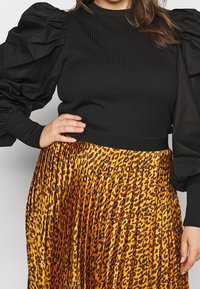 Maglione nero a coste con maniche in tessuto nero voluminoso, abbinato a una gonna gialla plissettata con un motivo maculato marrone.