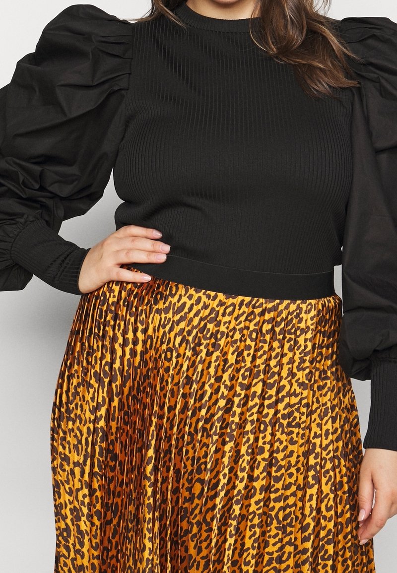 Maglione nero a coste con maniche in tessuto nero voluminoso, abbinato a una gonna gialla plissettata con un motivo maculato marrone.