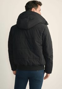 Czarna pikowana kurtka z kapturem, z poziomymi przeszyciami i elastycznymi mankietami. Gładka tekstura i luźny krój.