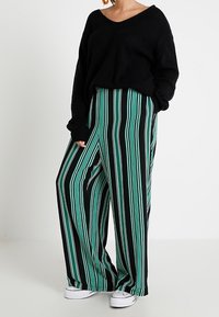 Pull noir oversize en maille avec col en V, associé à un pantalon large à jambes larges, ample, rayé verticalement en noir, sarcelle et blanc.