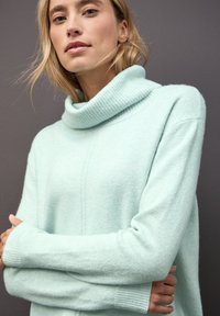 Jasno miętowy sweter z golfem, z ryżowym splotem przy kołnierzu i mankietach, o miękkiej fakturze i luźnym kroju; posiada delikatny detal szwu.
