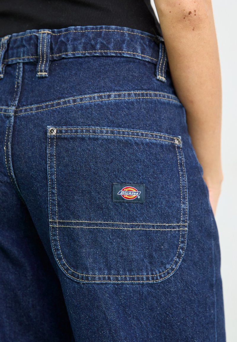 Pantaloni in denim blu con vita cucita, tasca posteriore con patch del logo e dettagli di cucitura dorata a contrasto.