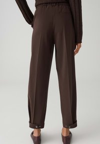 Bruine broek met wijde pijpen en een elastische tailleband, voorzien van voorzakken en omslagen met knoopsluiting. Soepele stofafwerking.