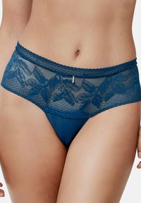 Teal kantene string met bloempatroon, doorschenkende bovenband en een massieve onderkant. Heeft golvende randen en een kleine zilveren accent aan de voorkant.