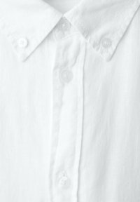 Hvid skjorte med knapper, knaplukning ved kraven og synlige knapper langs frontklappen.