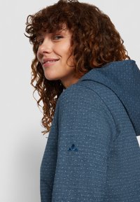Hooded sweatshirt in textured dark blue fabric with white dots, featuring embroidered logo on the sleeve and a relaxed fit.