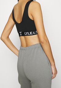 Sort bomulds sports-bh med bred stropdesign og en struktureret talje, som prydes af det hvide "LYLE & SCOTT" logo. Sættes sammen med grå joggingbukser.