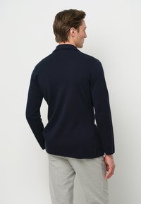 Pullover della marina in maglia con colletto morbido e maniche lunghe. Presenta una finitura testurizzata e fessure laterali all'orlo.