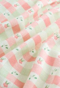 Tissu doux avec un motif vichy pêche et crème, orné de petites fleurs roses et de feuilles vertes dispersées dessus.