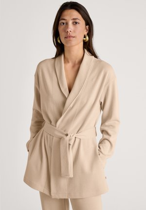 Beige Wickelrobe aus weichem Stoff mit Schalkragen, gebundenem Gürtel und Taschen. Strukturierte Oberfläche mit lässiger Passform.