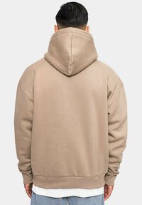 Beige, übergroßer Hoodie mit einer großen, doppellagigen Kapuze, gerippten Bündchen und Saum. Glatte Textur, minimale Nähdetails, schlichtes Design.