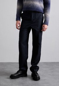 Pantalon noir, ajusté avec une texture lisse et une coupe décontractée. Détail avec une taille subtile et associé à des chaussures en cuir noires.