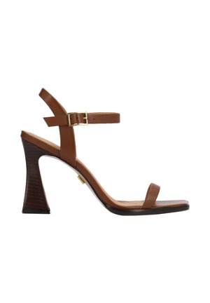 Rjava usnjena sandaleta z visokim petom, z zaponko okoli gležnja, zlato sponko, odprtimi prsti in rahel leseni peti na belem ozadju.